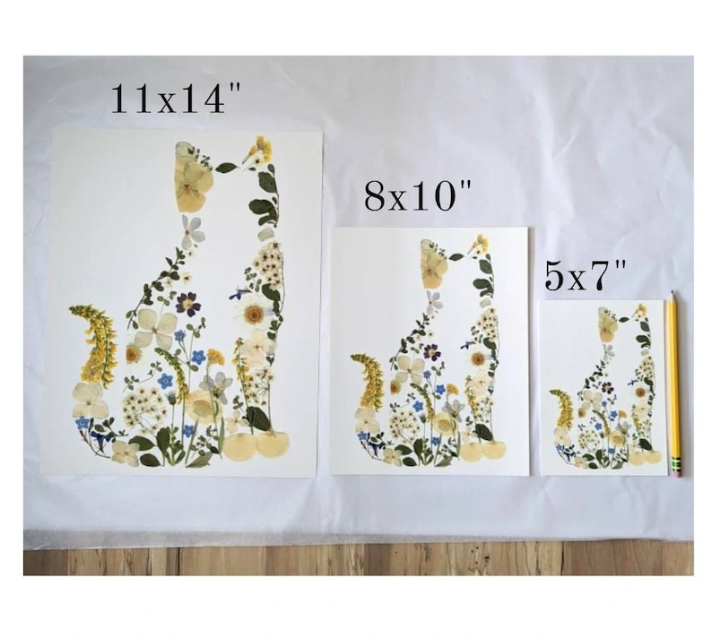 May include: Three different sizes of pressed flower art prints featuring a cat silhouette made of flowers. The prints are 11x14 inches, 8x10 inches, and 5x7 inches.