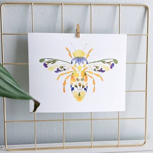 May include: A bee made of pressed flowers, with yellow, orange, purple, and white petals. The bee is on a white background.