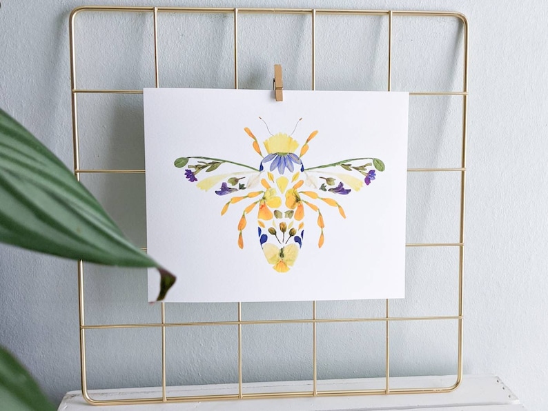 May include: A bee made of pressed flowers, with yellow, orange, purple, and white petals. The bee is on a white background.