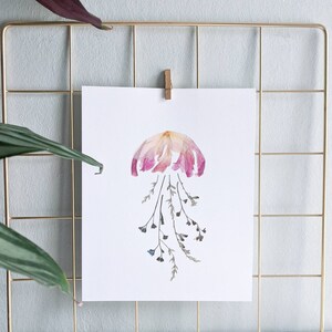 May include: A pink and white dried flower arrangement in the shape of a jellyfish with dried green stems and blue flowers hanging down.