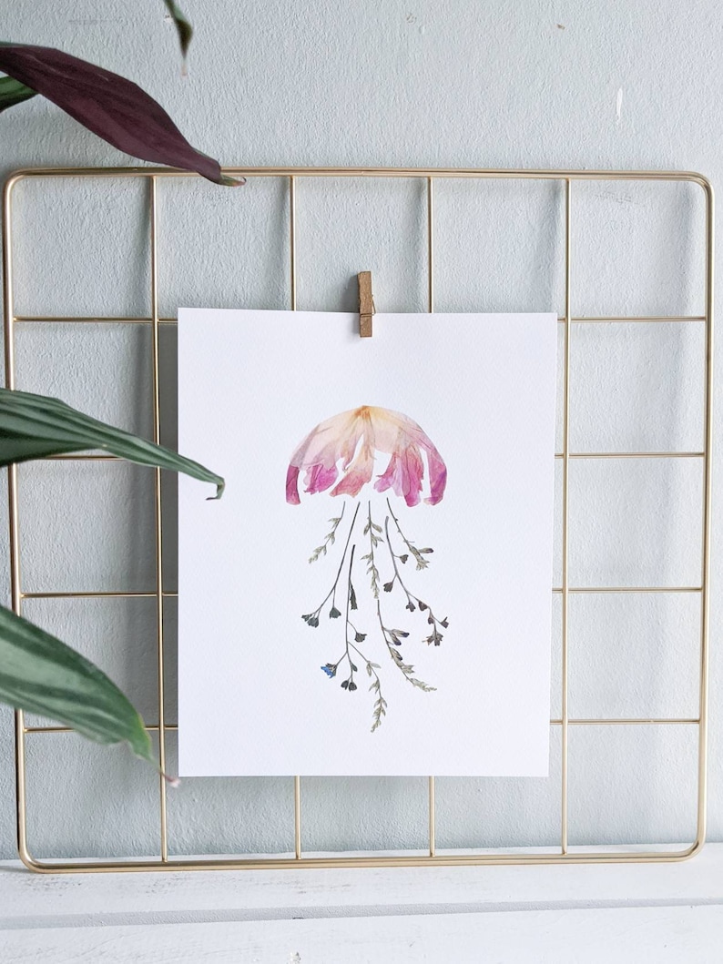 May include: A pink and white dried flower arrangement in the shape of a jellyfish with dried green stems and blue flowers hanging down.