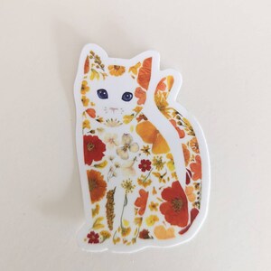 May include: A white cat sticker with a floral design. The cat is made up of pressed flowers in shades of orange, yellow, and red.