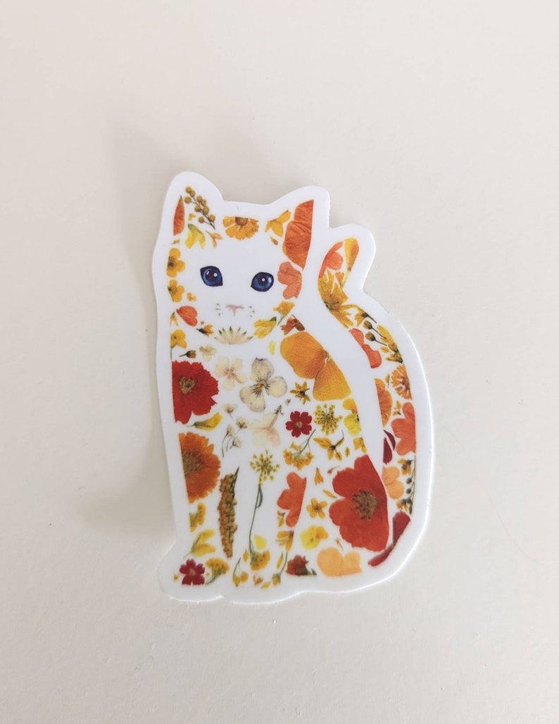 May include: A white cat sticker with a floral design. The cat is made up of pressed flowers in shades of orange, yellow, and red.