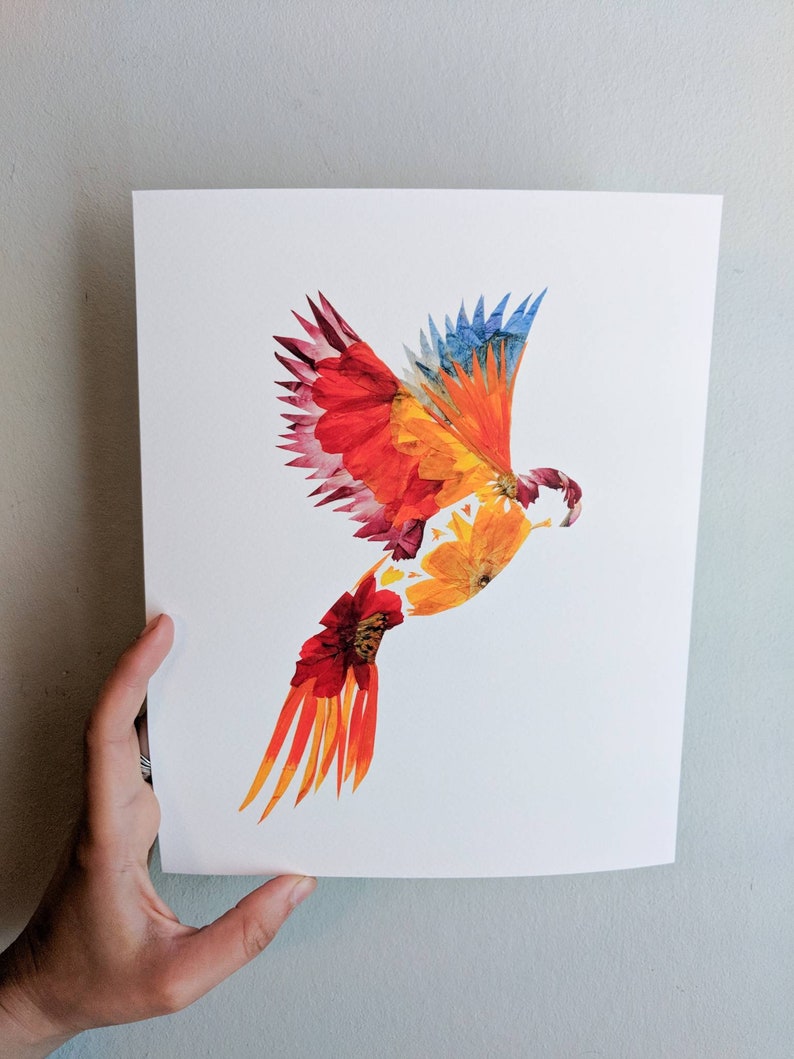 May include: A colorful bird made from pressed flowers. The bird is in flight with its wings spread wide. The bird is made from red, orange, yellow, and blue flowers.