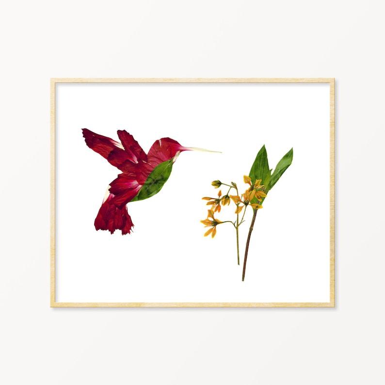 May include: A framed print featuring a hummingbird silhouette crafted from red flower petals and green leaves. The hummingbird is positioned near a sprig of yellow flowers with green leaves, all set against a white background.