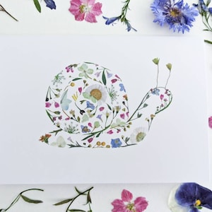 May include: A white card with a snail made of pressed flowers. The snail is a light pink, purple, and blue color.