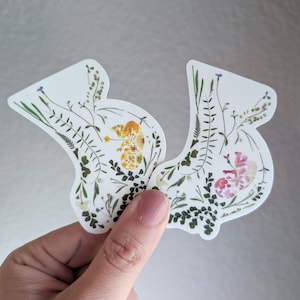 May include: Two white stickers with pressed flowers and leaves. The left sticker features yellow flowers and green leaves. The right sticker features pink flowers and green leaves.