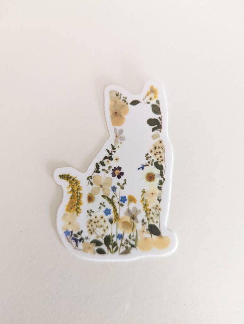 May include: A white cat silhouette sticker with pressed flowers and leaves in shades of yellow, white, blue, and green.