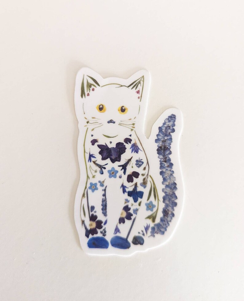 May include: A white cat sticker with a blue and purple floral design. The cat is sitting with its tail curled behind it.