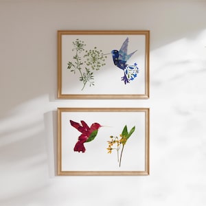 May include: Two framed art prints featuring hummingbird designs. One print shows a blue hummingbird with floral accents and a sprig of greenery. The other print displays a red hummingbird with green accents and yellow flowers.