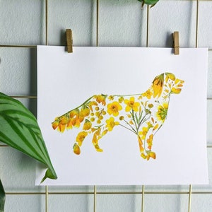 May include: A white print of a dog silhouette filled with yellow flowers and greenery. The artwork is clipped to a gold wire grid with a wooden clip. A green plant with striped leaves is in the foreground.
