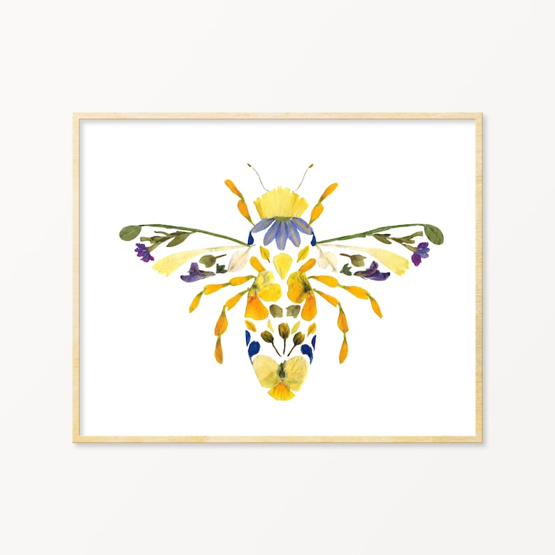 May include: A bee made of pressed flowers. The bee is yellow, blue, and purple. The bee is framed in a light wood frame.
