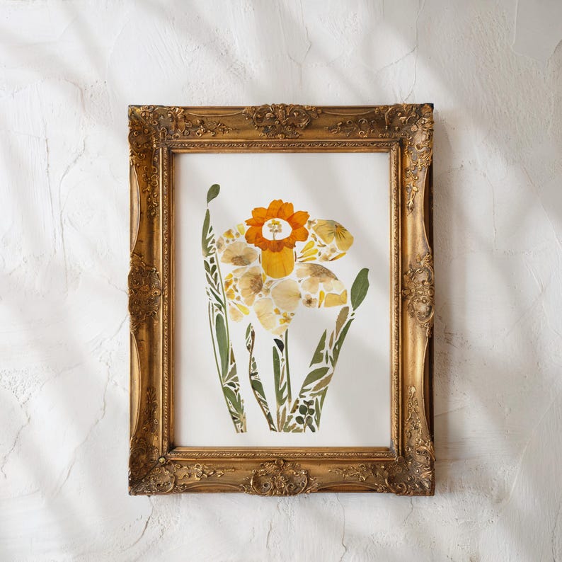 May include: A framed print of a daffodil flower made from pressed flowers. The flower is yellow and orange and is surrounded by green leaves. The frame is gold and has a decorative design.