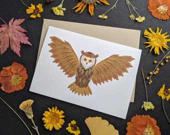 May include: A white card featuring a brown owl crafted from pressed flowers and leaves. The owl has a white face with black eyes and a yellow beak. The card is surrounded by dried flowers and leaves.