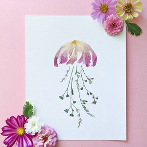 May include: A pink and white flower arrangement in the shape of a jellyfish with green stems and blue flower buds on a white background.