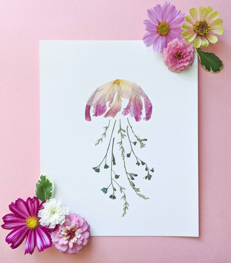 May include: A pink and white flower arrangement in the shape of a jellyfish with green stems and blue flower buds on a white background.