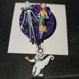 May include: A purple glitter badge reel featuring a Jack Skellington and Sally charm. The charm is a 3D representation of the characters from the Nightmare Before Christmas film. The reel also has a Zero charm attached to it.