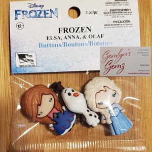 May include: Three Frozen character buttons: Elsa, Anna, and Olaf. The buttons are made of plastic and feature the characters' faces and outfits. The buttons are packaged in a clear plastic bag with a header card that says "Disney Frozen" and "3 pc/pz".