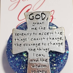 May include: A silver cross charm with a blue glitter background. The cross has the text "GOD, grant me the serenity to accept the things I cannot change, the courage to change the things I can, and the wisdom to know the difference AMEN".