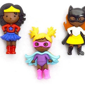 Pode incluir: Três figuras de super-heróis. Uma usa um top vermelho com uma saia azul e botas vermelhas. Outra tem uma roupa roxa com uma capa azul clara e botas rosa. A terceira tem uma máscara, capa e botas pretas com uma saia amarela.