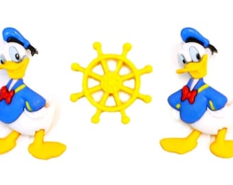 Puede incluir: Dos personajes de pato de dibujos animados amarillos y azules con un timón de barco amarillo en el centro. Los patos llevan camisas de marinero azules con ribetes amarillos y corbatas de lazo rojas.