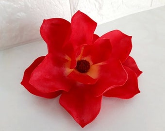 Op de afbeelding: Een enkele, grote, rode kunstbloem met een gele kern. De bloem heeft meerdere bloemblaadjes en is gemaakt van een zacht, stofachtig materiaal.