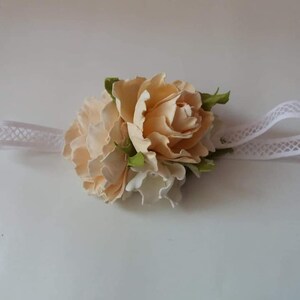May include: A white headband with a delicate lace pattern, adorned with a cluster of three cream-colored fabric flowers.
