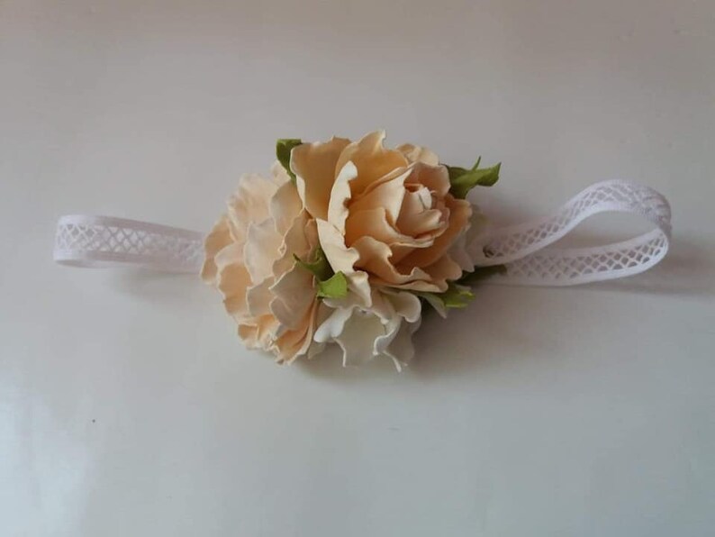 May include: A white headband with a delicate lace pattern, adorned with a cluster of three cream-colored fabric flowers.
