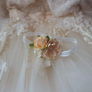 May include: A white headband with a delicate lace trim and a peach-colored flower embellishment.