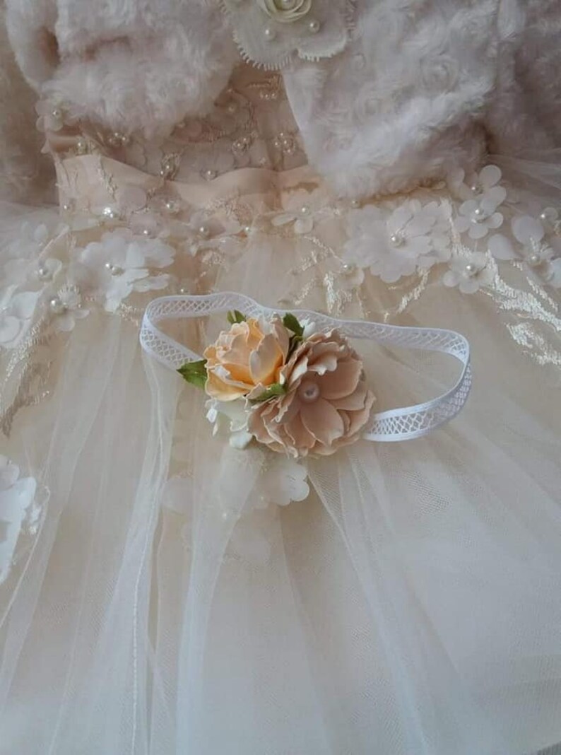 May include: A white headband with a delicate lace trim and a peach-colored flower embellishment.