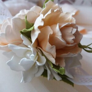 May include: A delicate floral arrangement featuring peach and white fabric flowers. The flowers are arranged in a cluster and have a realistic appearance.