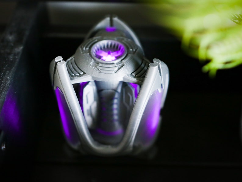 May include: A silver and purple 3D printed object with a glowing purple light inside. The object has a geometric design and appears to be a futuristic or sci-fi themed item.