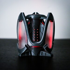 May include: A black and gray 3D printed object with a red glow. The object has a geometric design with multiple points and a central cylinder.
