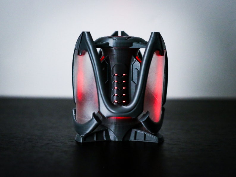 May include: A black and gray 3D printed object with a red glow. The object has a geometric design with multiple points and a central cylinder.