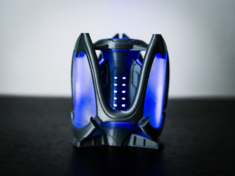 May include: A black 3D printed object with a geometric design. The object is illuminated with blue lights, creating a futuristic and modern aesthetic.