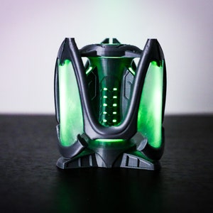 May include: A 3D printed, black and green, futuristic-looking object with a glowing green light inside.