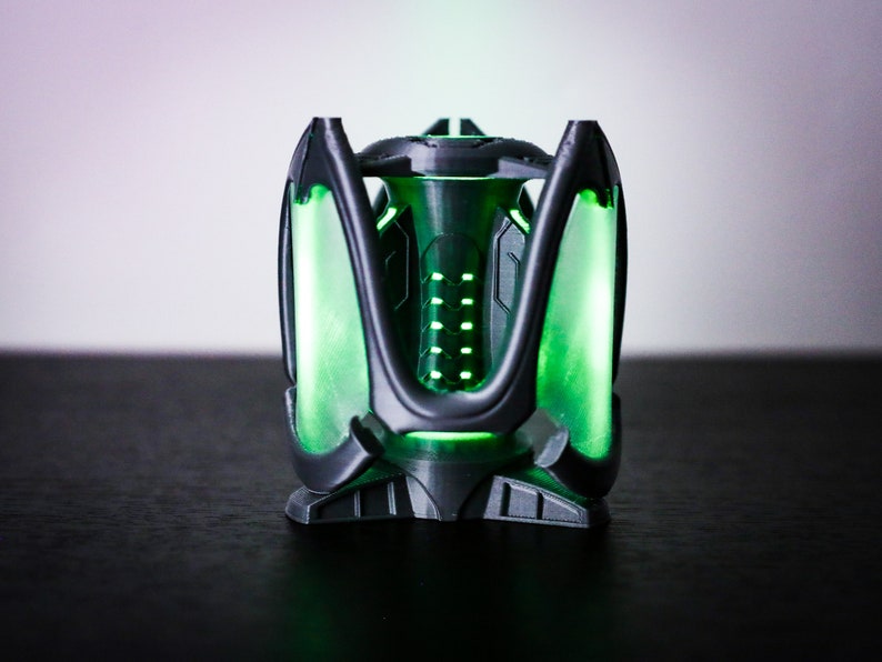 May include: A 3D printed, black and green, futuristic-looking object with a glowing green light inside.