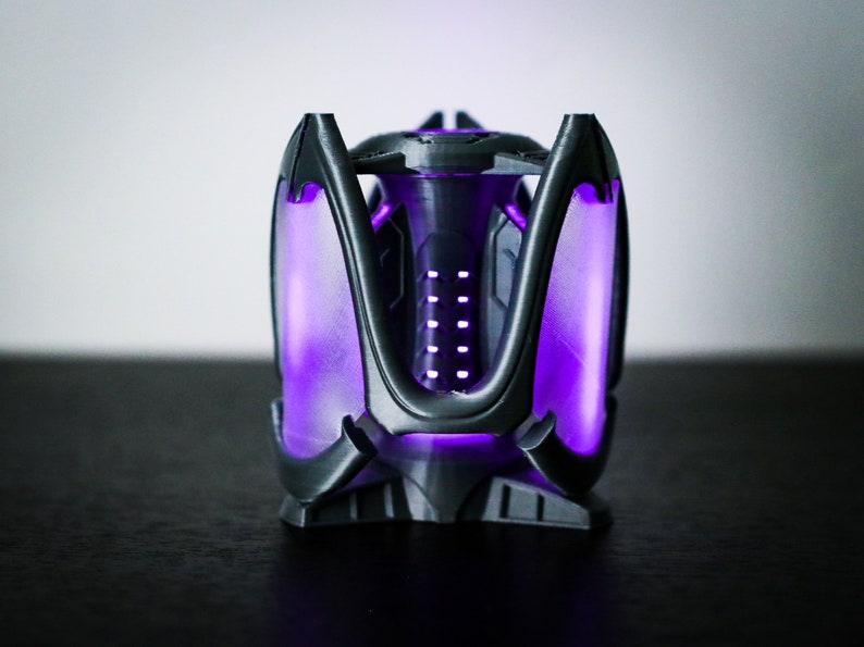 May include: A black 3D printed object with a purple glow. The object has a geometric design with a central column and multiple arms.