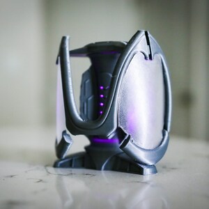 May include: A gray 3D printed object with a geometric design. The object has a translucent panel that glows purple.