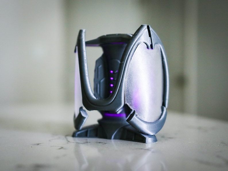 May include: A gray 3D printed object with a geometric design. The object has a translucent panel that glows purple.