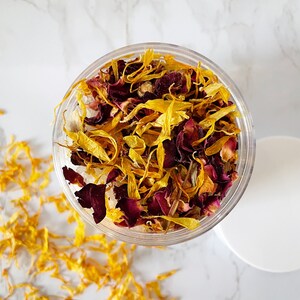 May include: A glass jar filled with dried yellow and red flower petals. The petals are a mix of yellow calendula and red rose petals.