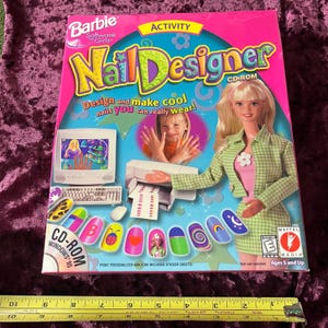 May include: A Barbie Nail Designer CD-ROM box with a pink background. The box features a Barbie doll, a computer, and nail designs. The text reads "Design and make cool nails you can really wear!" and "Print personalized nails on included sticker sheets!"