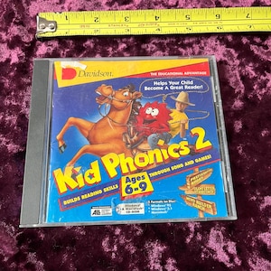 May include: A Kid Phonics 2 CD-ROM in a clear plastic case. The cover features a cartoon horse and a red monster, with the title in large yellow letters. The text reads "Builds Reading Skills" and "Ages 6-9".
