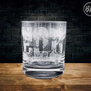 以下が含まれることがあります： 頭蓋骨と交差した骨の彫刻が施された透明なガラスのタンブラー。デザインはグラス全体に繰り返されています。