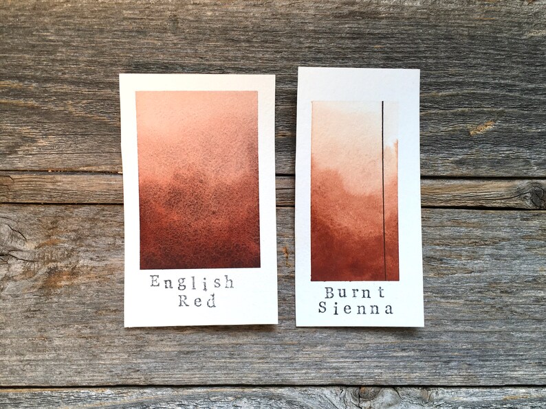 May include: Two watercolor paint swatches on white cardstock. The left swatch is labeled "English Red" and is a reddish-brown color. The right swatch is labeled "Burnt Sienna" and is a darker brown color.