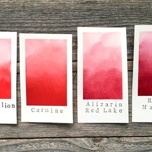 Op de afbeelding: Vier aquarelverfstaaltjes op witte kaartjes, die een verloop van licht naar donker laten zien. De staaltjes zijn gelabeld met "Vermiljoen", "Karmijn", "Alizarinroodmeer" en "Rozenmadder".