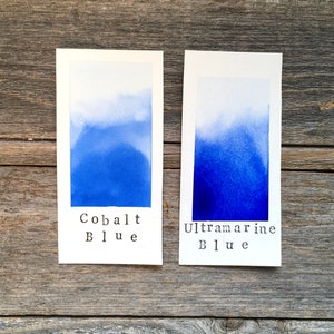 May include: Two watercolor swatches on white cardstock, one labeled "Cobalt Blue" and the other "Ultramarine Blue". The swatches show a gradient from light to dark blue.