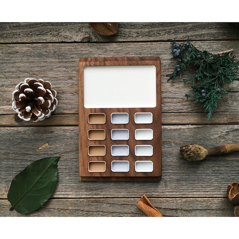 Może przedstawiać: Drewniany kalkulator z białym wyświetlaczem i brązowymi i białymi przyciskami. Kalkulator znajduje się na drewnianej powierzchni.