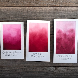Op de afbeelding: Drie aquarelverfstaaltjes op wit papier, met de labels "Quinacridone Magenta", "Rose Madder" en "Quin. Pink Madder".