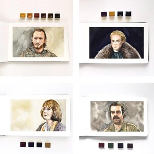 May include: A collection of four watercolor portraits in sketchbooks, each accompanied by small paint pans. The paintings depict individuals with distinct features, including a bearded person, a blonde person in fur, a person with glasses, and a mustachioed person.